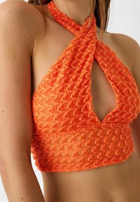Top holgado naranja brillante con un patrón texturizado y ondulado. Presenta un escote en V profundo y tirantes cruzados, fabricado con tejido ligero.