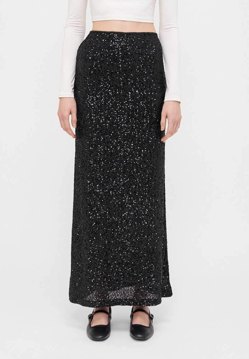 Zwarte maxi rok met pailletten en een aansluitende silhoeet, met een gestructureerd oppervlak en een gladde tailleband. Gekleed met een wit langemouwtop.