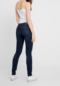 Smala blå jeans med medelhögt midjeavstånd, tillverkade av denimtyg. De har bakfickor och diskreta sömdetaljer. Kombinerat med vita sneakers.