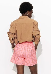 Chemise à rayures brunes avec manches retroussées et shorts roses ornés de motifs solaires et d'une taille froncée, vue de l'arrière.