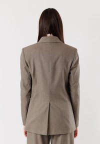 Blazer grigio su misura con colletto affilato, tessuto liscio e una sola apertura sul retro. Presenta spalle strutturate e una silhouette aderente.