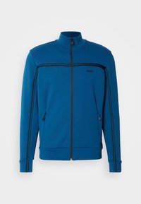 Blue zip-up jacket featuring a high collar, black accent stripes, and side pockets; made from smooth, lightweight fabric.