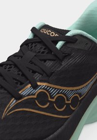 Μαύρο αθλητικό παπούτσι με μαύρα κορδόνια, χρυσό και φωτεινό μπλε λογότυπο, και φωτεινό μπλε επένδυση γύρω από τον γιακά του αστραγάλου.