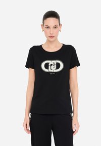 Camiseta de algodón negra con un diseño de logo metálico central adornado con strass. Manga corta y cuello redondo.
