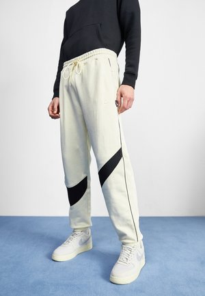 Vaaleat kermaiset joggerit mustilla yksityiskohdilla, sivuviivoilla ja joustavalla vyötäröllä. Yhdistetty vaaleanharmaisiin Nike-tossuihin.