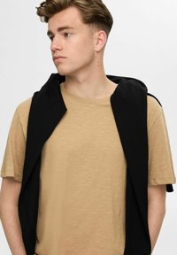 Beige textured t-shirt with short sleeves, paired with a black hoodie draped over the shoulders. Minimalist casual design.