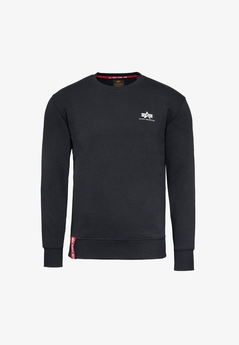 Sweat-shirt noir à col rond avec le logo Alpha Industries sur la poitrine et une étiquette rouge près de la ceinture sur le côté avant gauche.