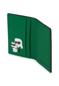 Zaļš ādas maciņš atvērts, kurā attēlots karikatūras tēls melnā uzvalkā un saulesbrillēs kopā ar baltu kaķi, kuram arī ir saulesbrilles.