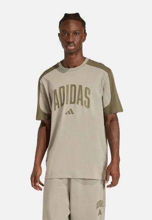 Uomo con capelli intrecciati che indossa una maglietta beige Adidas e pantaloncini abbinati con pannelli a contrasto color oliva su spalle e maniche.