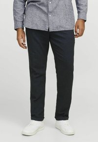 Mörkblå, slim-fit-byxor i strukturerad tyg, kombinerade med vita sneakers. Byxorna har ett subtilt randmönster och standardfickor.