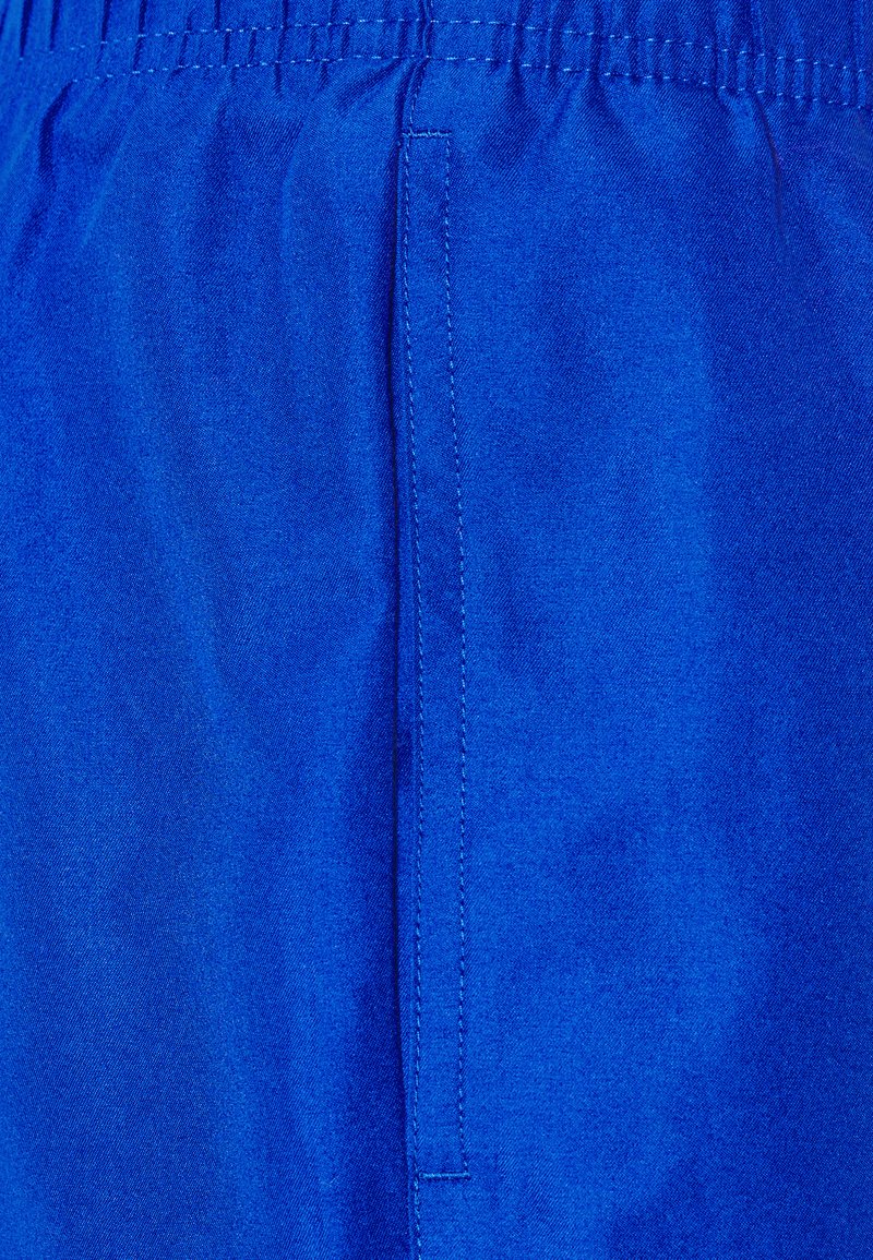 Tissu bleu avec une texture lisse, doté d'une taille élastique. Une couture verticale court le long du côté, mettant en valeur le design.