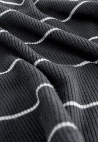 Tissu texturé noir avec des rayures ondulées blanches, présentant une surface côtelée et une apparence douce, avec des plis créant de la profondeur et du mouvement.