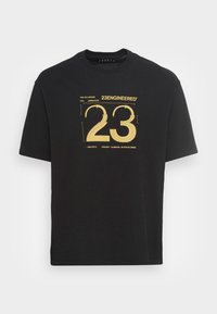 Černé tričko s krátkým rukávem s žlutou grafiku ve technickém stylu "23" a textem "23Engineered" umístěným na středu přední části.