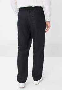 Zwarte linnen broek met een elastische tailleband, rechte pijpen en een achterzak, gecombineerd met witte sneakers. Gestructureerde stofafwerking.