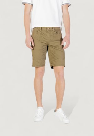 Shorts cargo en verde oliva con un corte relajado, con múltiples bolsillos y detalles de costura. Llevados con una camisa blanca de manga corta y zapatillas blancas.