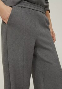 Pantaloni grigi in felpa realizzati in un tessuto morbido, caratterizzati da tasche laterali, una vestibilità rilassata e dettagli di cucitura delicati per una struttura aggiuntiva.