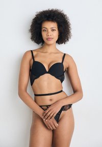 Soutien-gorge en dentelle noire avec des bonnets rembourrés, des bretelles réglables et un string en dentelle assorti. Texture douce avec des détails intricats et des accents de matériel minimal.