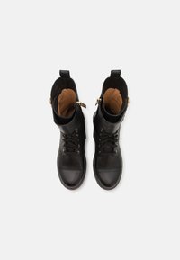 Sorte skinnanklestøvler med rund tå, snøring foran, gullfarge accenter og brettede kanter. Innvendig foret med beige stoff.