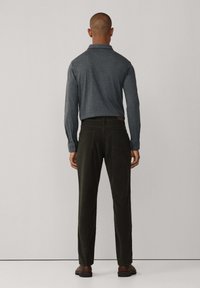 Camisa polo de manga larga gris oscuro combinada con pantalones verdes oscuros. El atuendo presenta un corte clásico y una textura de tela suave. Calzado casual completa el look.