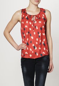 Blusa rossa senza maniche con scollatura a barchetta, dettaglio a fiocco e un motivo di pois bianchi e blu navy. Tessuto liscio con leggero lucido.