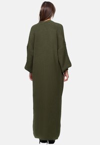 Lång olivgrön stickad kofta med överdimensionerade ärmar, texturerad tyg och en rak silhuett som sträcker sig ner till anklarna.