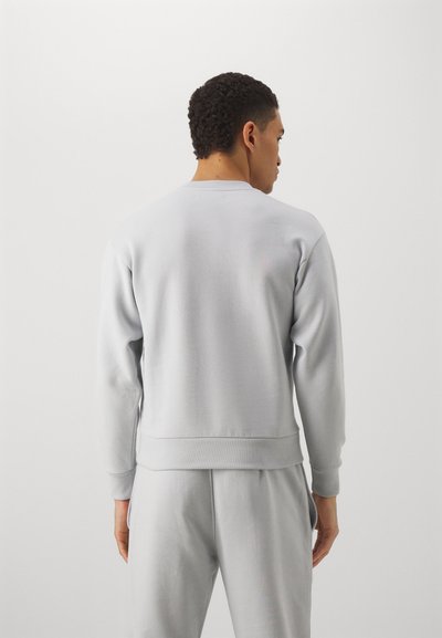 Sudadera gris con cuello redondo y puños de canalé, hecha de una tela suave. Presenta un ajuste relajado y una textura suave.