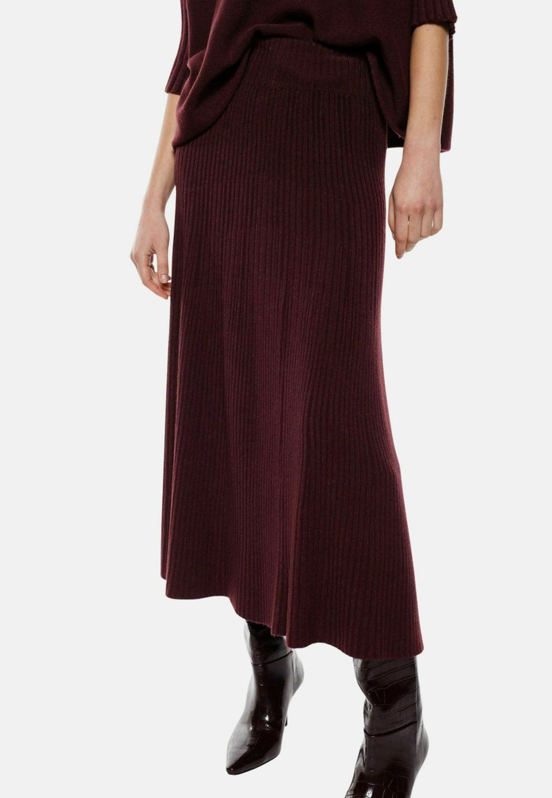 Gonna maxi in magenta a costine con vita aderente e silhouette fluida, abbinata a stivali neri lucidi al ginocchio.