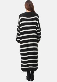 Schwarz-weißer gestreifter Oversize-Pullover mit geripptem Halsauschnitt, langen Ärmeln und einer lockeren Passform, die bis zur Mitte der Waden reicht. Stricktextur.