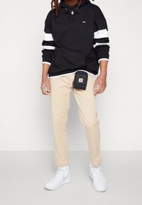 Black hooded sweatshirt with white stripes, khaki pants, and white sneakers. Includes a small black pouch clipped to the pants.