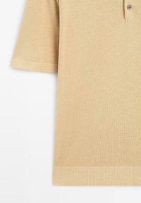 Polo shirt a maglia beige con colletto classico, maniche corte e dettagli a costine sulle maniche e sull'orlo. Un dettaglio con bottone.