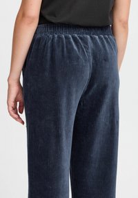 Granatowe sztruksowe spodnie o szerokich nogawkach. Posiadają elastyczną talię i pionową fakturę-żebrowanie. Widok z tyłu ukazuje gładkie linie.