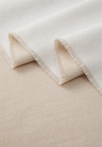 Beige og off-white stoflag, blød tekstur, med frynsede kanter og en glat finish. En neutral farvepalet med subtile nuancer.