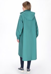 Türkiz vízálló kabát kapucnival, gumírozott mandzsettákkal és bő fazonnal. Hosszú szabás, tiszta, minimalista dizájn, látható rögzítők nélkül.
