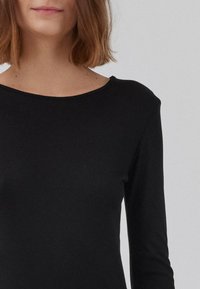 Crna bluza dugih rukava s okruglim izrezom, izrađena od glatkog, rastezljivog materijala; priljubljen dizajn, minimalno šavova vidljivih.