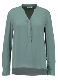 Langärmlige Bluse in hellem Türkis mit V-Ausschnitt, verdeckter Knopfleiste und einem leicht dunkleren, gestuften Saumdetail.