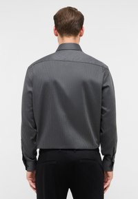 Heren langarmshirt in donkergrijs met een klein geometrisch patroon. Voorzien van een klassieke kraag en knopenmanchetten. Vloeiende textuur, getailleerde pasvorm.