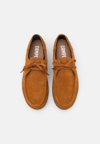 Scarpe in suede marrone con punta rotonda, suola piatta e lacci marroni. Presentano una superficie testurizzata e un'etichetta interna con il marchio "CAMPER".