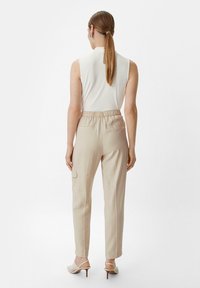Beżowe spodnie cargo o gładkiej teksturze, elastycznym pasie i bocznych kieszeniach. Noszone z białym topem bez rękawów i sandałami na obcasie.