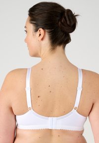 Sujetador blanco con tirantes ajustables y bordes festoneados, que presenta un cierre de gancho y ojal en la parte posterior. Tejido suave y diseño sencillo.