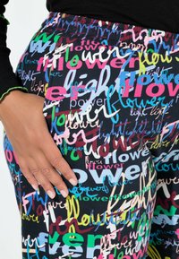 Multifarvede leggings med teksttryk, der indeholder "blomst" og "lys" i forskellige skrifttyper. Blødt, strækbart stof med elastisk talje.