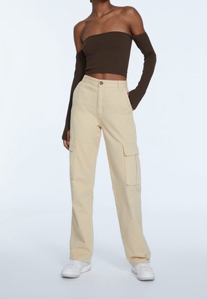 Pantalones cargo color beige con bolsillos laterales y un diseño de pierna recta, combinados con una blusa marrón sin hombros. Zapatillas blancas completan el look.