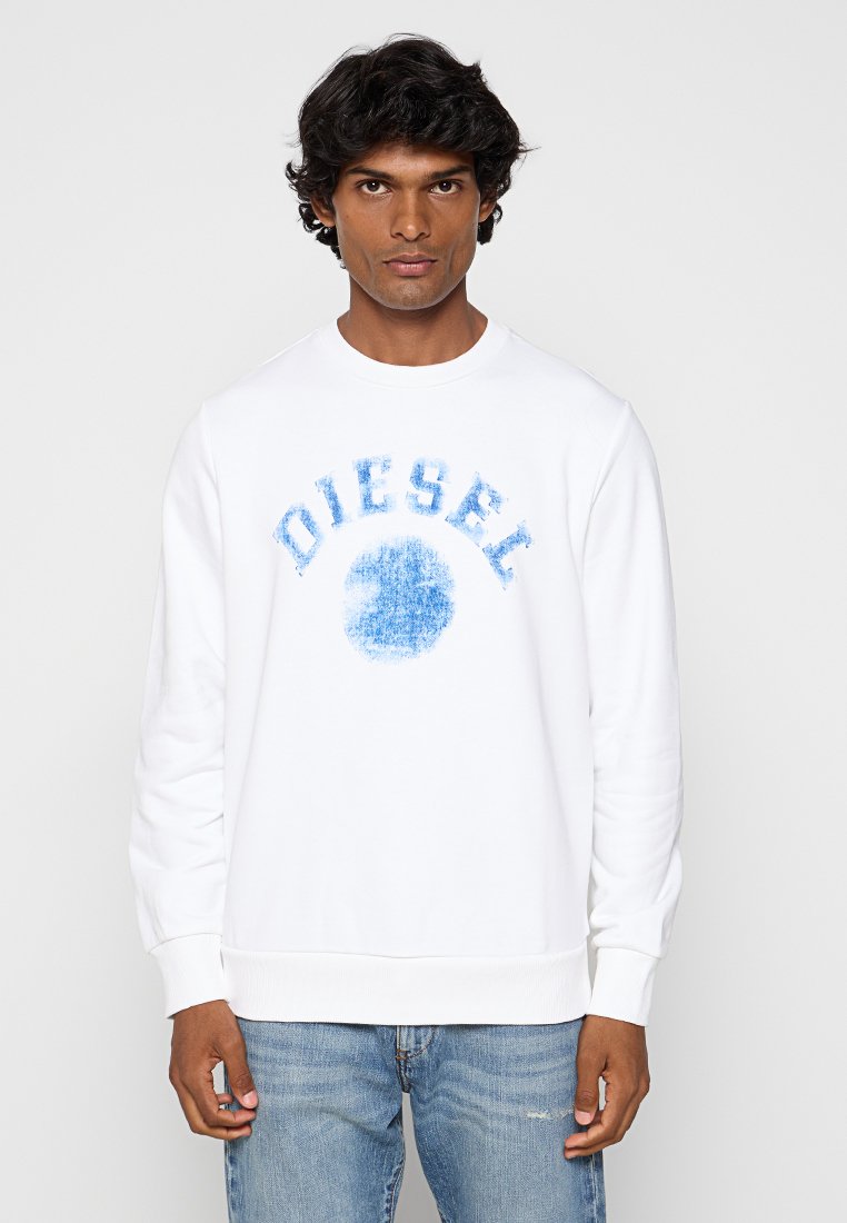 Felpa bianca con testo "DIESEL" blu e grafica circolare. Polsini e orlo a costine. Abbinata a jeans in denim blu chiaro.
