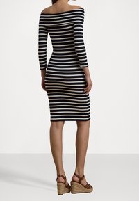 Proužkované šaty s odhalenými rameny, které mají námořnické a krémové horizontální pruhy, těsný střih, tříčtvrteční rukávy a délku ke kolenům.