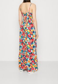 Robe maxi à fleurs avec dos smocké, bretelles fines et motifs multicolores vifs sur un fond sombre. Longueur au sol.