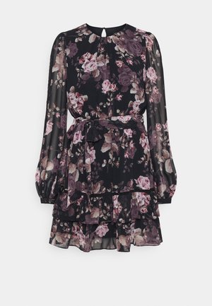 Blomstret kjole i sort gennemsigtigt stof med lange ærmer, lag med flæser og matchende bælte. Farverne inkluderer nuancer af pink og creme.