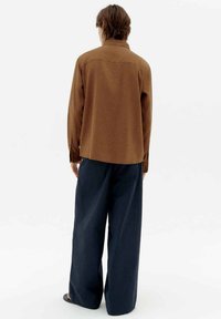 Brown button-up shirt with a straight cut, worn over wide-leg navy trousers. The shirt features long sleeves and a single back yoke.