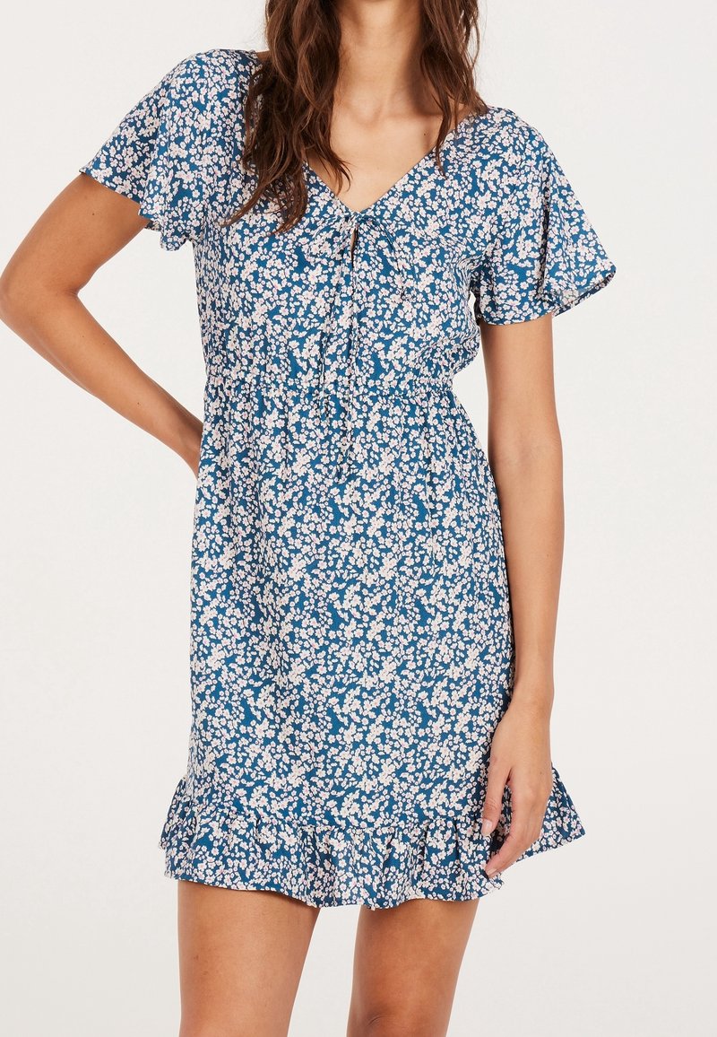 Robe fleurie en tissu bleu avec des manches courtes à volants et un col en V. Elle présente une taille cintrée et un ourlet à volants, ornée de petites fleurs roses.