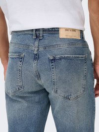 Vaqueros de mezclilla azul claro con un diseño deslavado, cinco bolsillos y una etiqueta rectangular de cuero en la cintura que muestra el nombre de la marca.