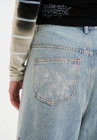 Svetle modré džíny z denimu mají květinový výšivkový design na zadní kapse. Tkanina má měkkou strukturu a klasický střih.