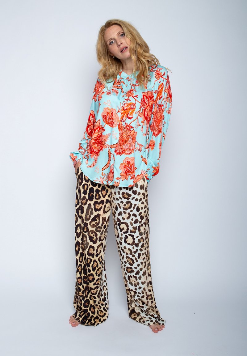 Bloemdruk blouse in turquoise met oranje bloemen, gecombineerd met beige en bruine panterprint broek. Zachte, vloeiende stoffen, losse pasvorm.